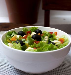 Delicious fresh salad with black olives, lettuce, and veggies in a white bowl indoors.